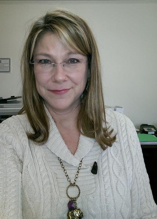 A woman wearing glasses and a necklace is smiling for the camera.