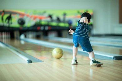 A young boy is bowling on a wooden bowling alley.