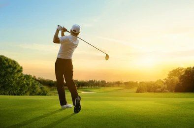 A man is swinging a golf club on a golf course at sunset — Bali Hi Motel In Tuncurry, NSW