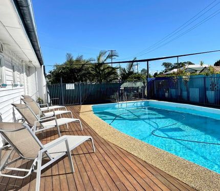 Pool with deck and lounge chairs, blue water, sunny day.