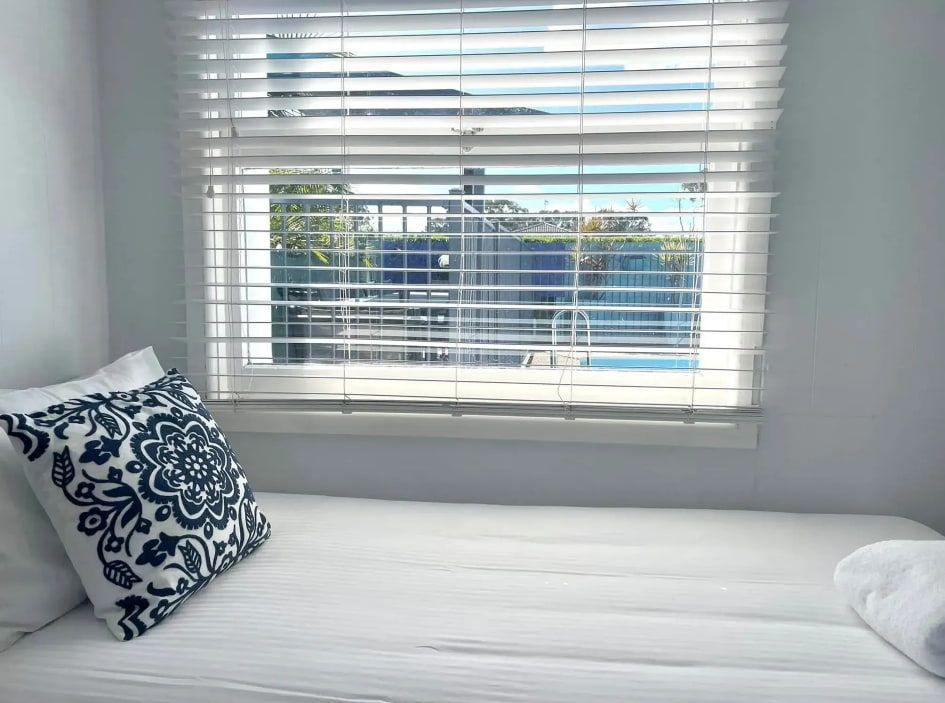 A Bed With a Blue and White Pillow in Front of a Window With Blinds — Bali Hi Motel In Tuncurry, NSW