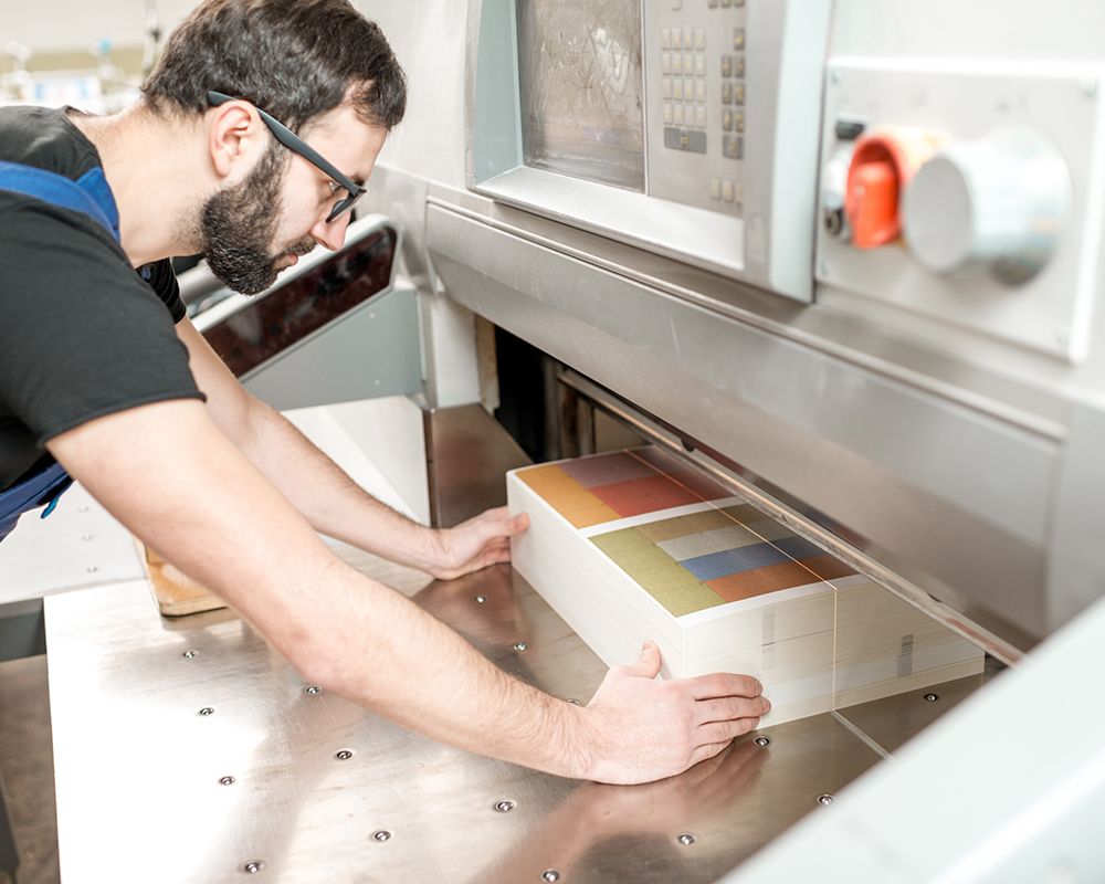 Commercial printing at Debbie’s Copy Shop in Colleyville, TX, with a man aligning paper for precision cutting. Commercial printing at Debbie’s Copy Shop in Colleyville, TX, with a man aligning paper for precision cutting.