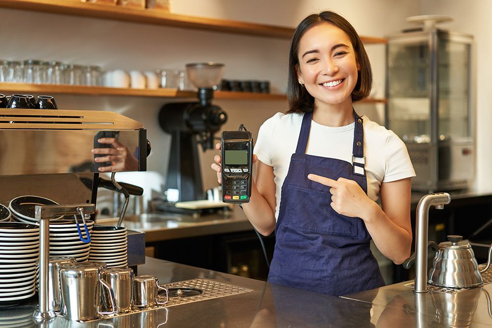 A woman is standing at a counter in a restaurant holding a credit card machine.