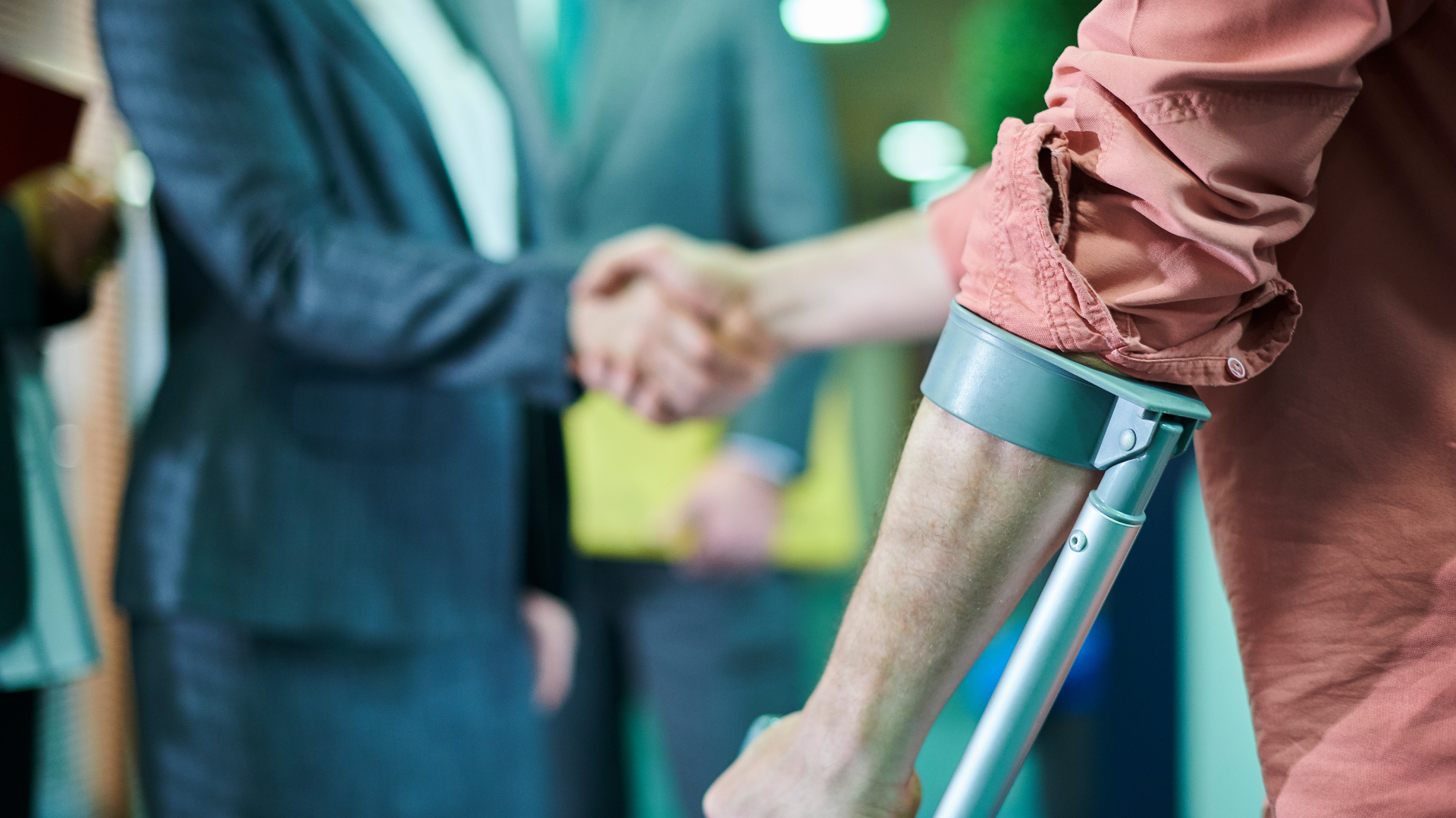 Person with arm crutches shaking hands with another person in a blurred indoor setting