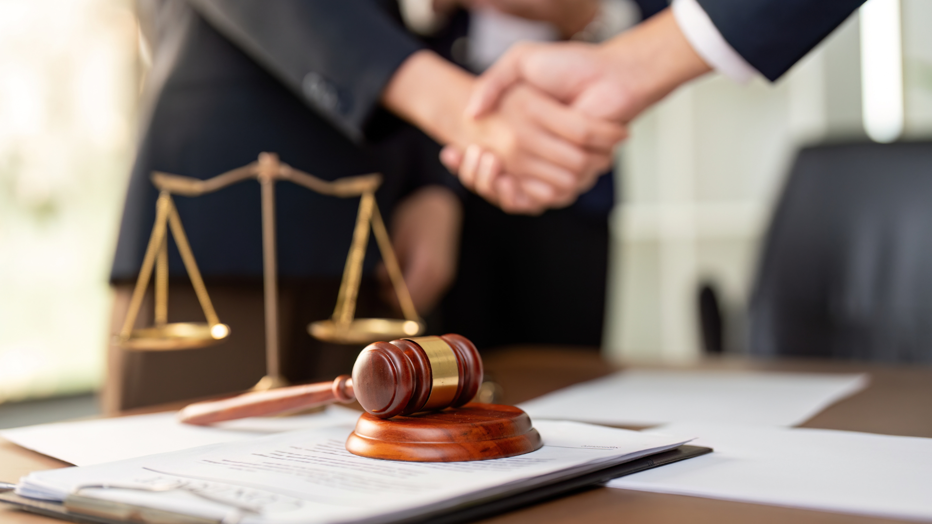 Lawyer’s gavel on desk with businesspeople shaking hands in the background