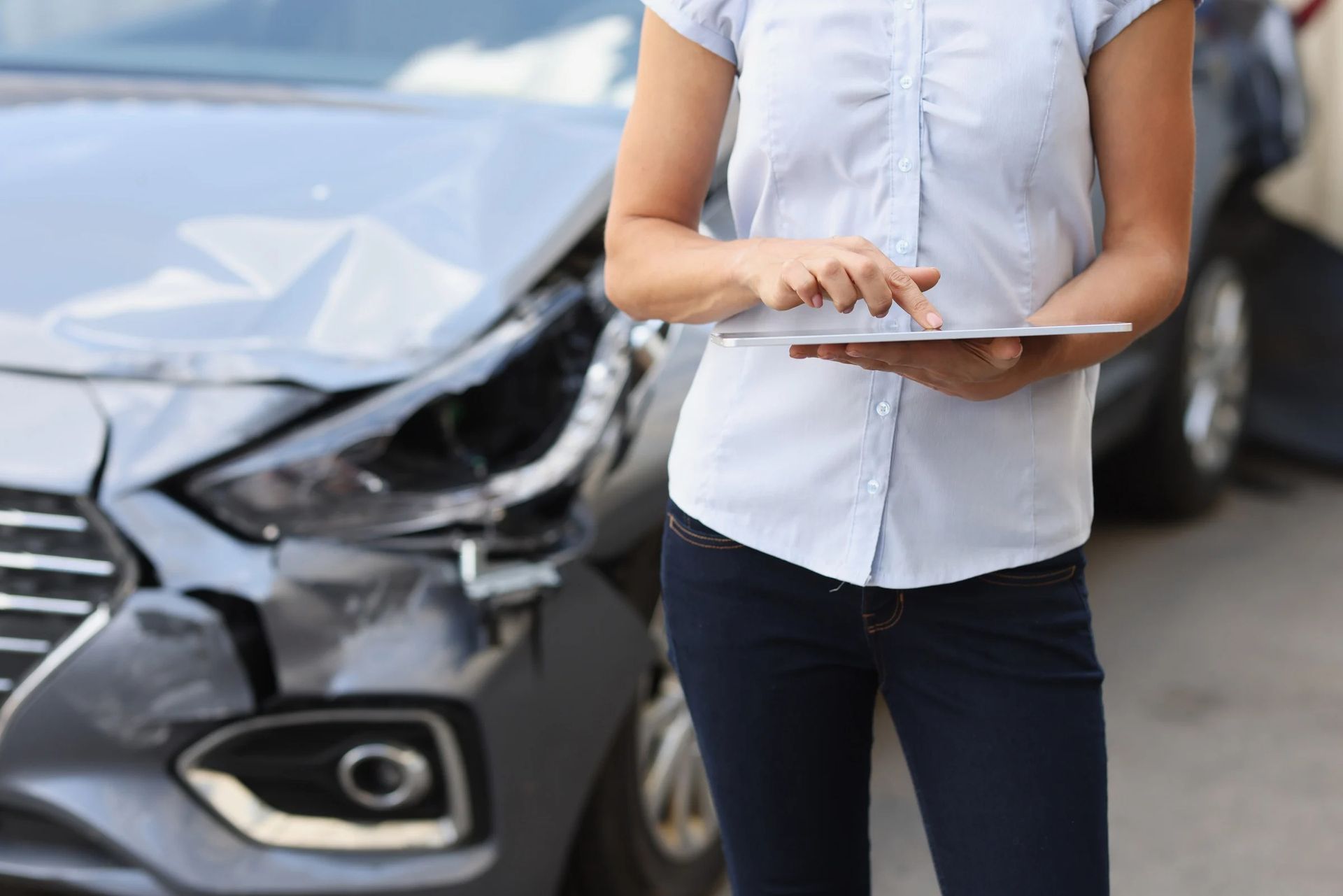 Two people inspect a red car outdoors, one holding a tablet and the other using a phone.