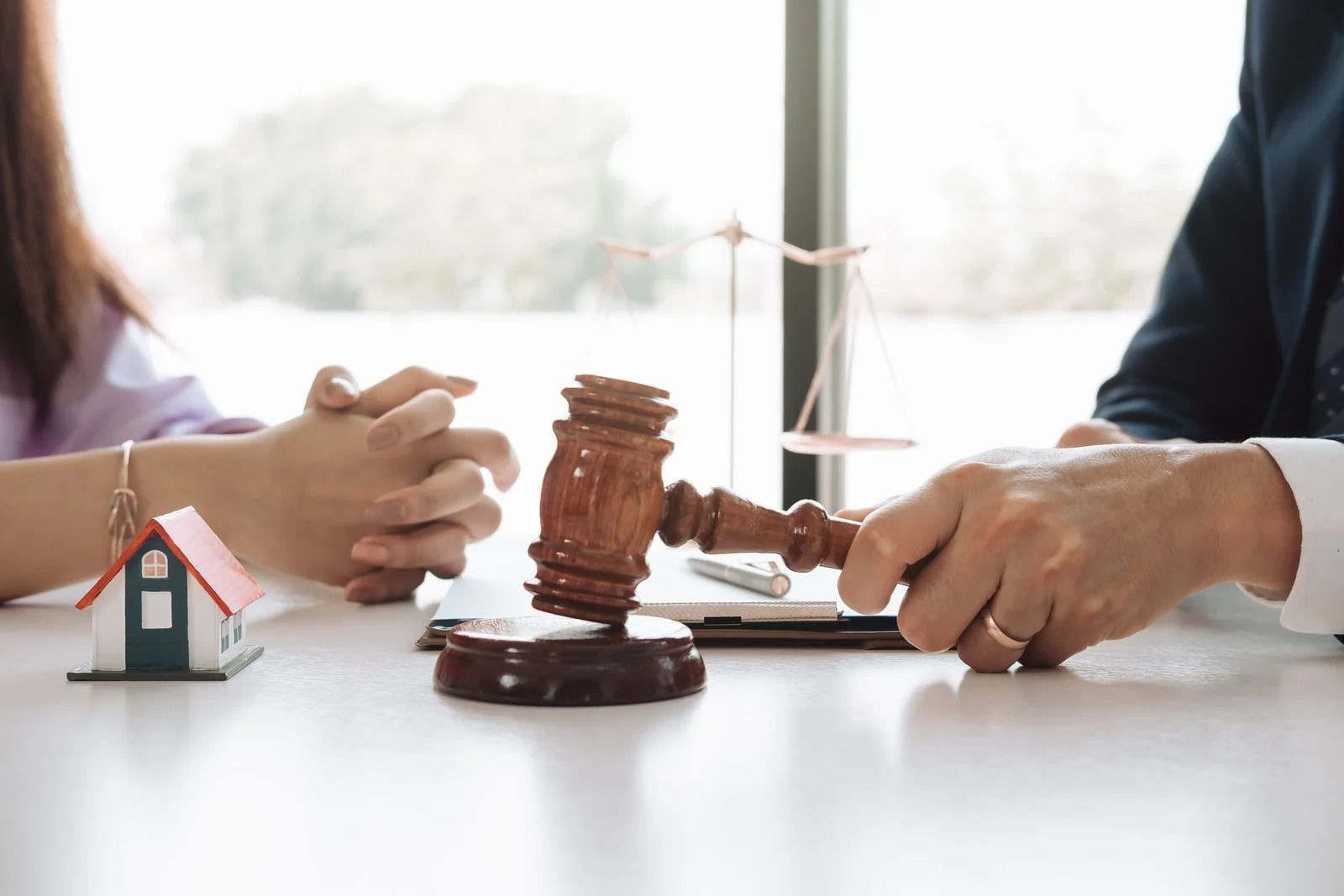 Lawyer in red blazer holding a gavel beside a small house model on a desk