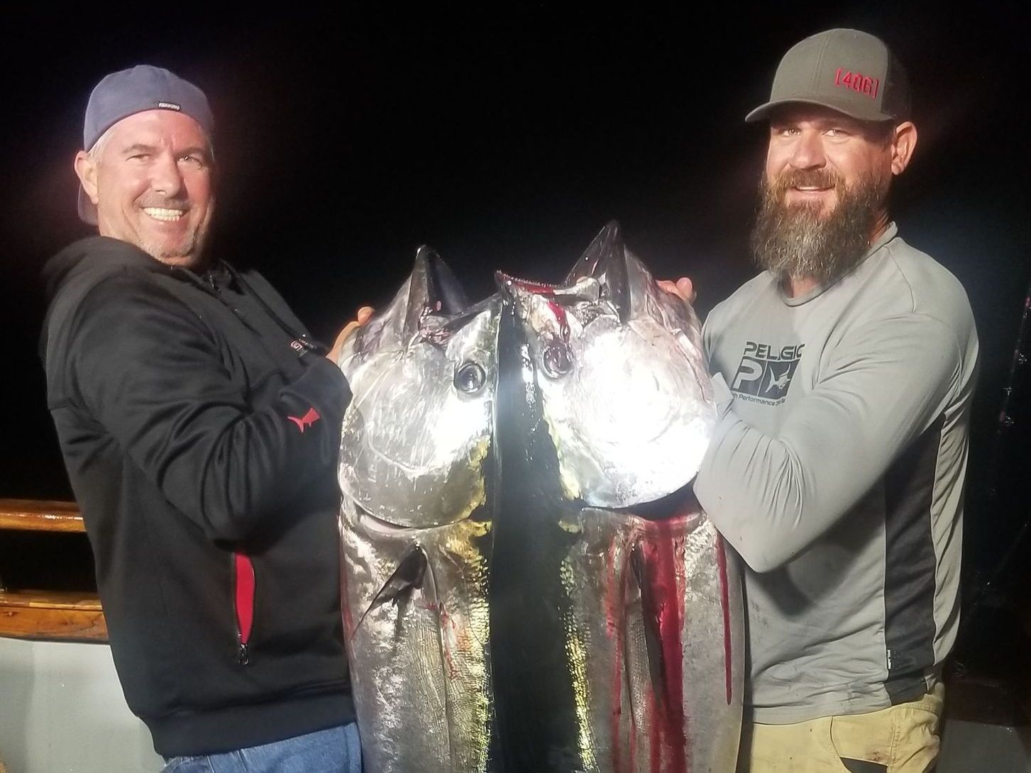 Two men are standing next to each other holding large fish.