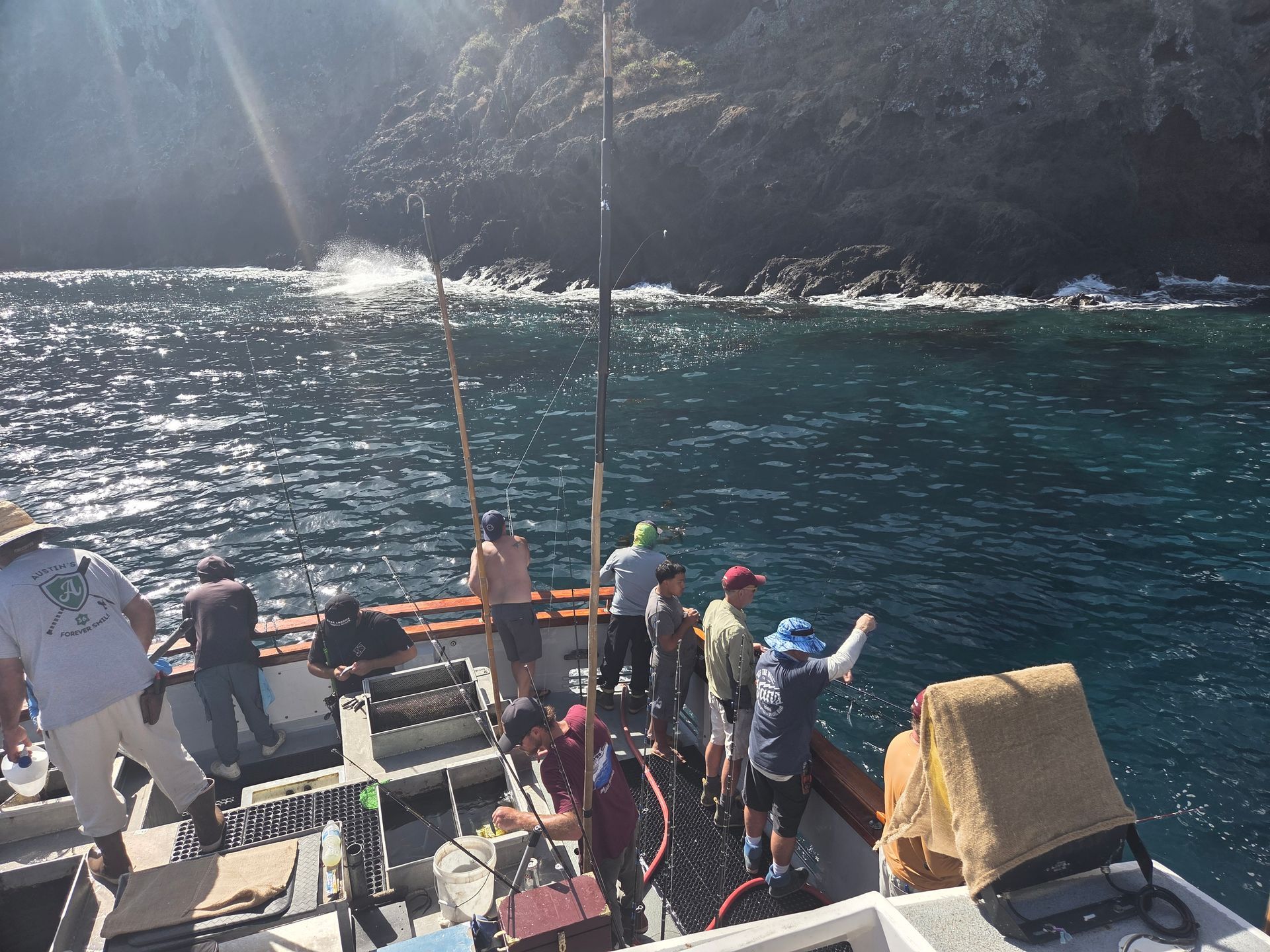 People fishing from a boat near a rocky coastline; sunny day.
