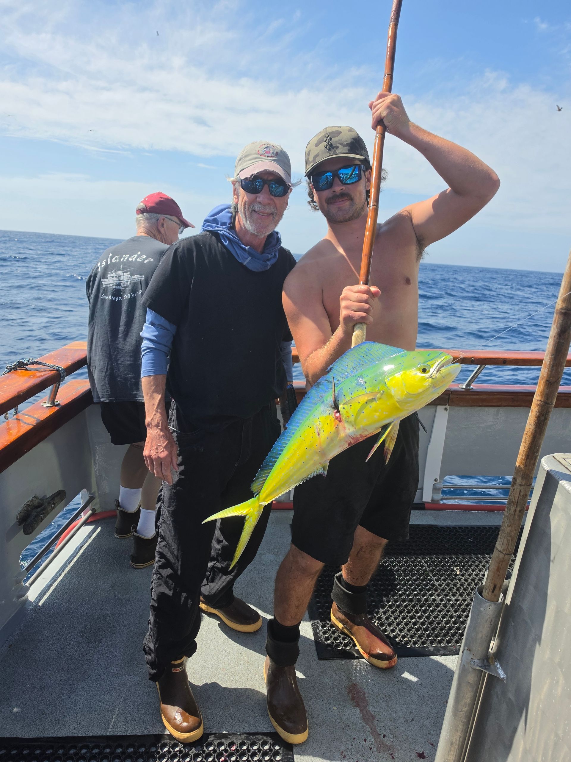 Two anglers on a boat holding a bright yellow fish, with the ocean in the background.