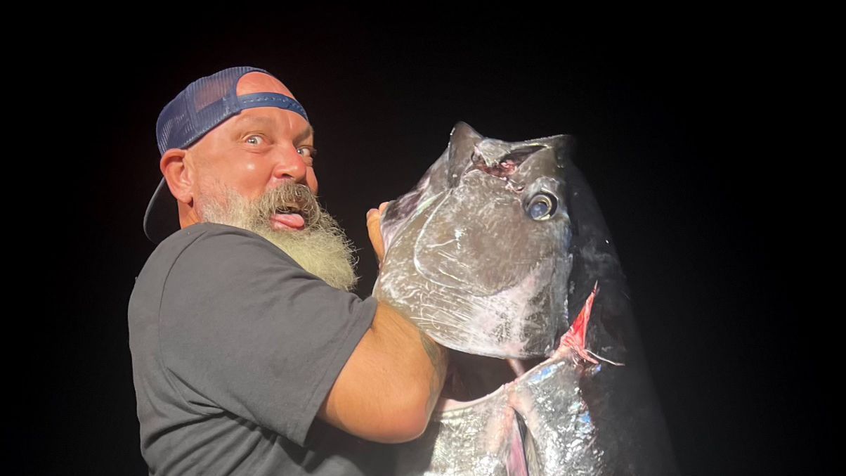 A man with a beard is holding a large fish in his hands.