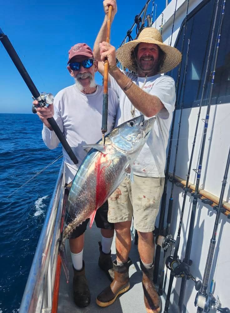 Two men on a boat hold up a freshly caught tuna. Sunny day, blue water.