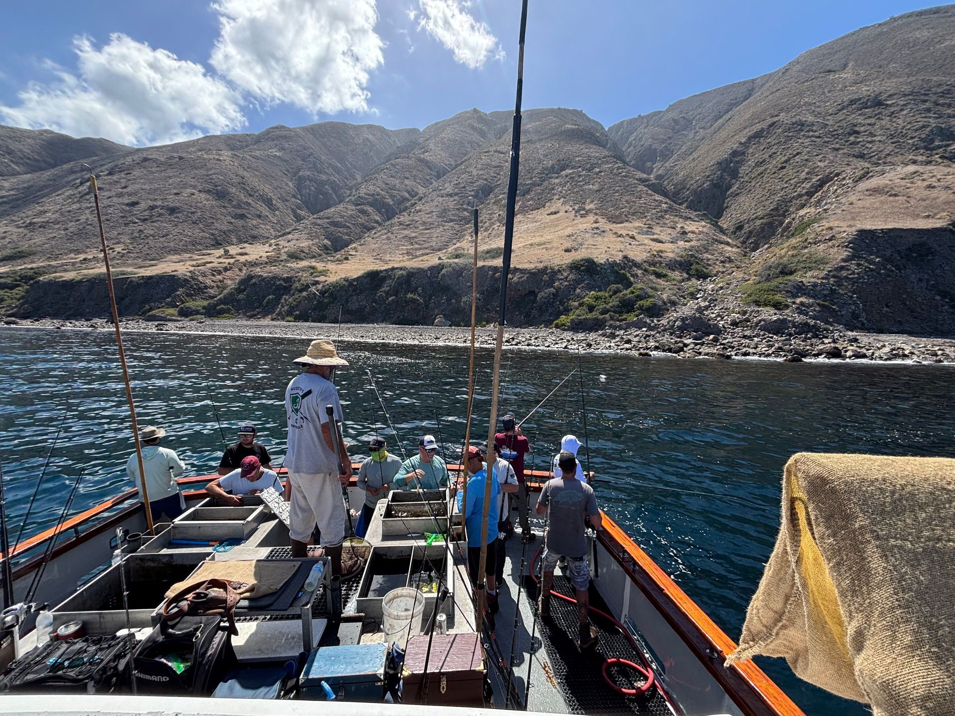 People fishing on a boat in front of a rocky mountain. Blue water, sunny day.