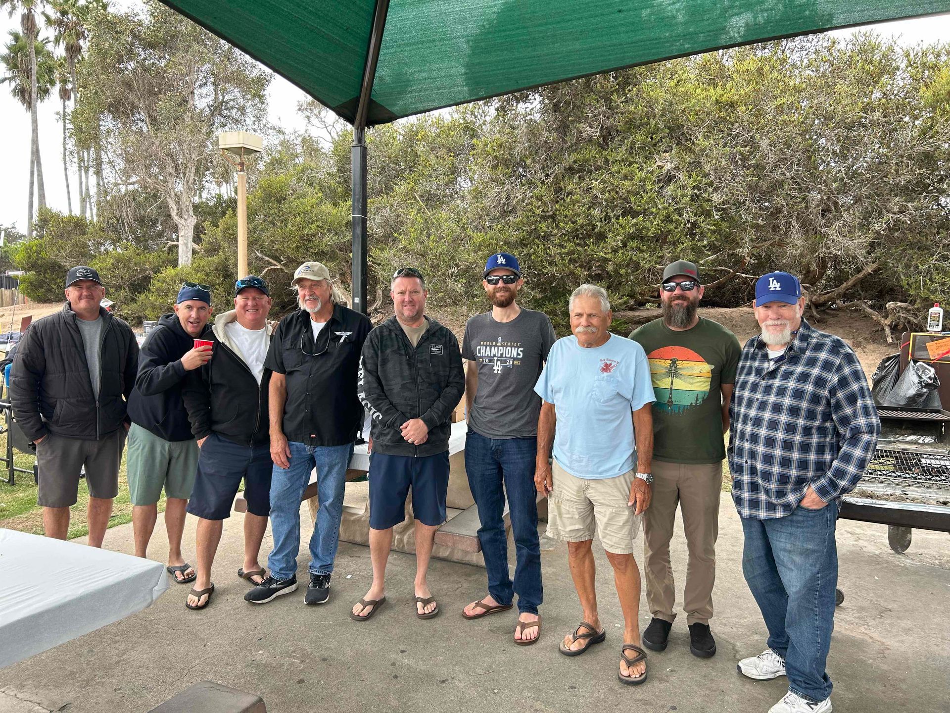A group of men are standing next to each other under an umbrella.