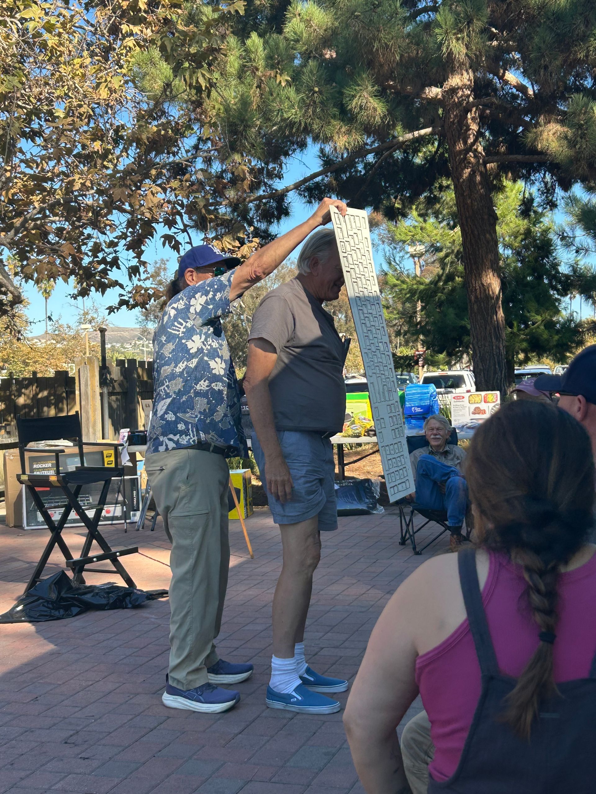 Person holding a patterned banner over another person outdoors, possibly measuring height or making a presentation.