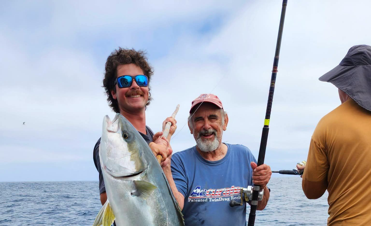 Three people on a boat hold up a large fish while fishing at sea.