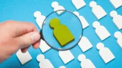 Hand holding magnifying glass over a green icon among white icons on blue background
