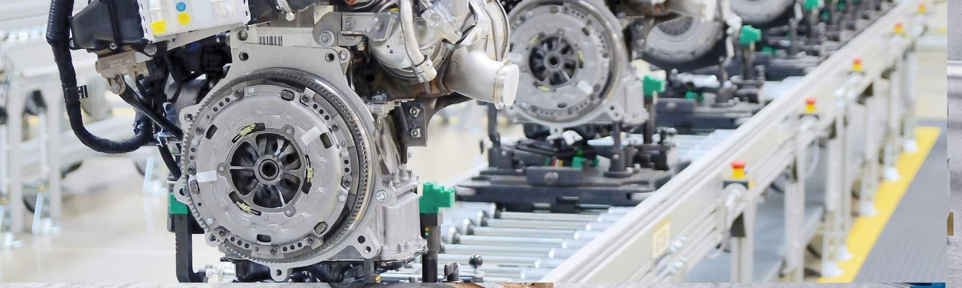 Car engines move along an industrial assembly line, showcasing metallic mechanical components in a factory setting.