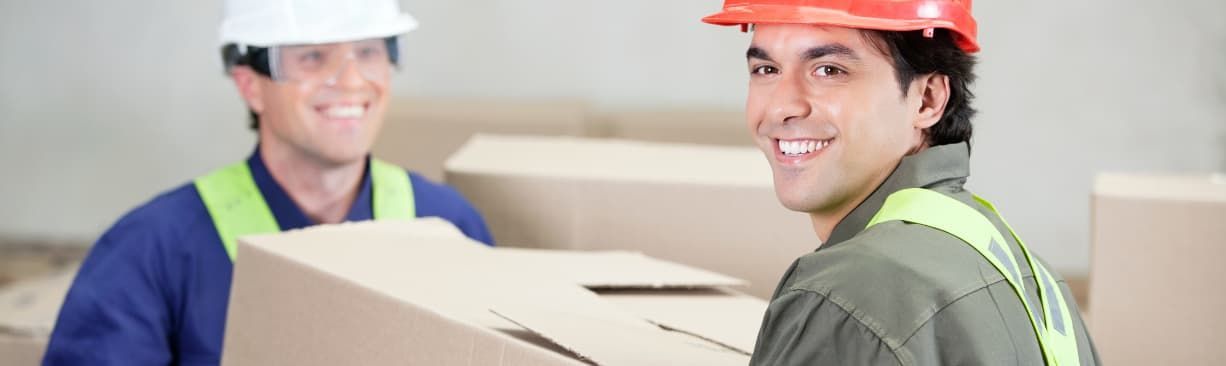 Two construction workers in hard hats carrying a large box indoors