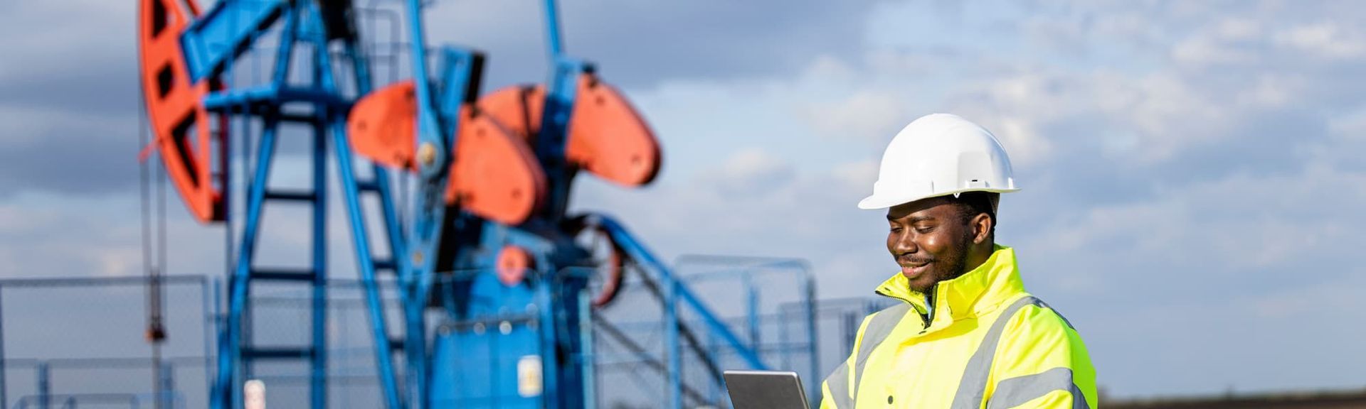 Oil worker in white hard hat and neon vest near blue drilling equipment outdoors