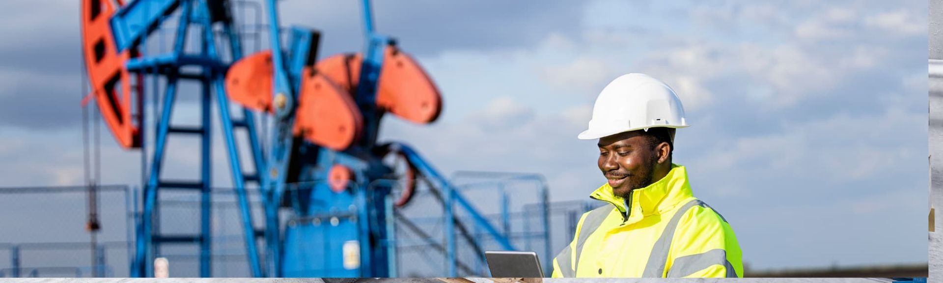 Oil worker in white hard hat and neon vest near blue drilling equipment outdoors