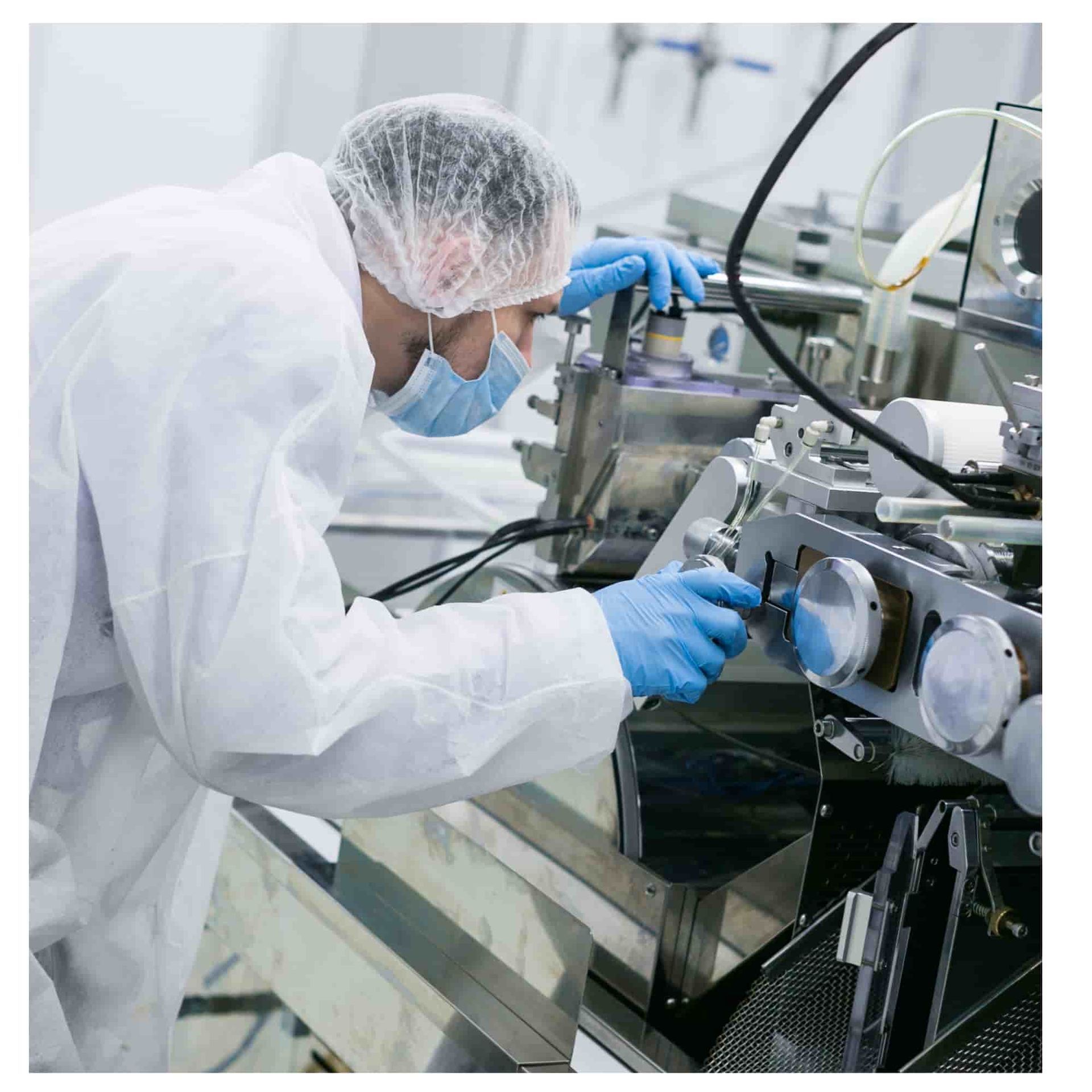 Technician in white protective suit and blue gloves adjusts machinery in a clean manufacturing lab