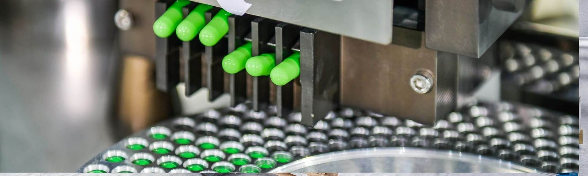 Automated machinery filling a metal tray with bright green capsules in a pharmaceutical manufacturing facility.