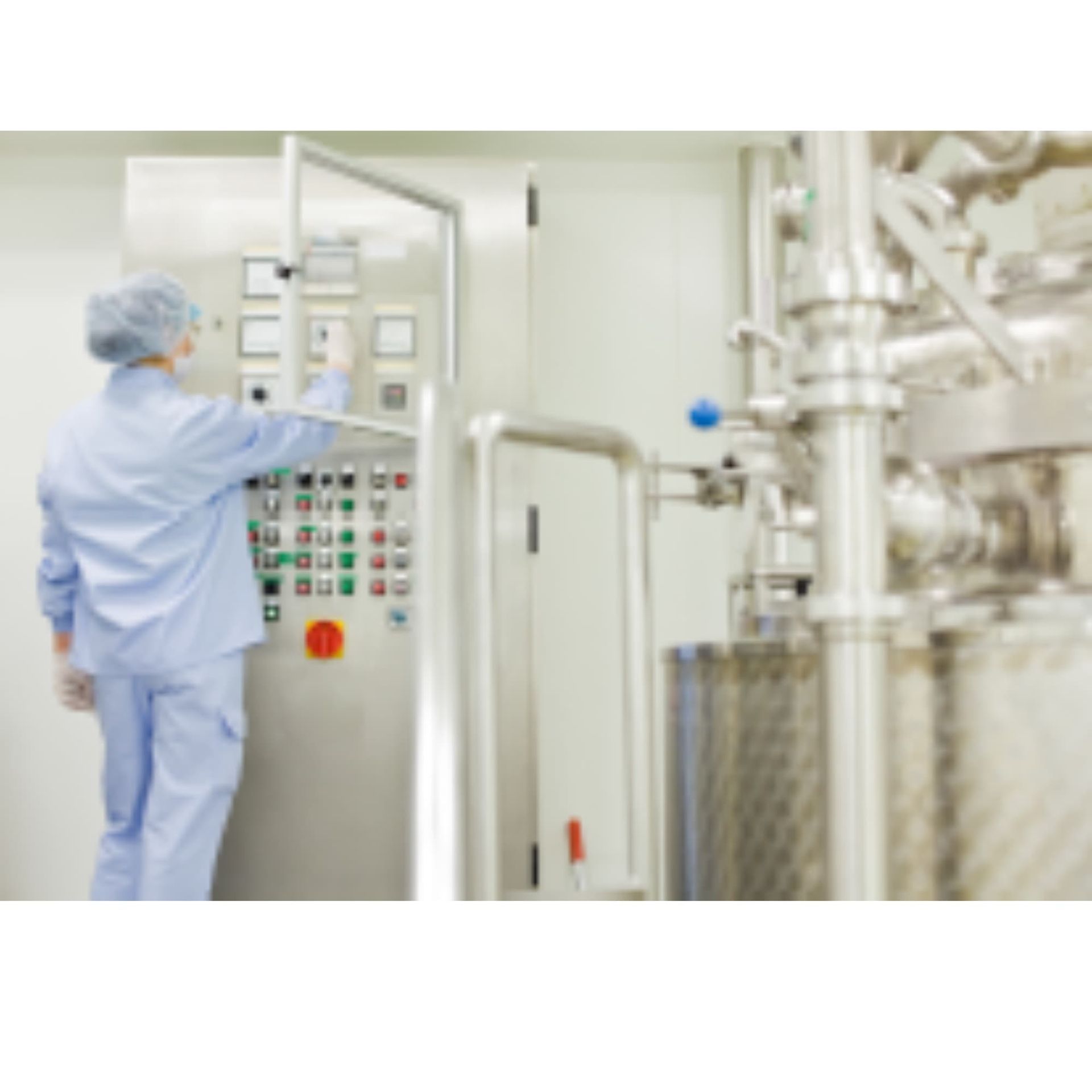 Technician in blue scrubs operating a control panel in a clean industrial facility