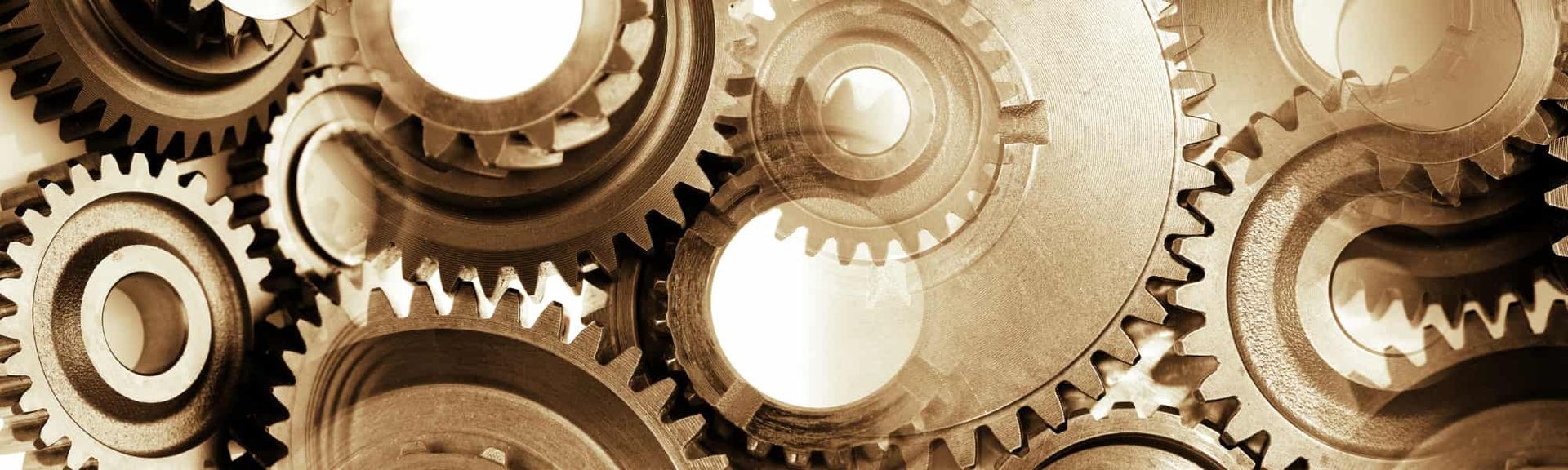 A collection of interlocking metallic mechanical gears shown in a close-up, sepia-toned view.