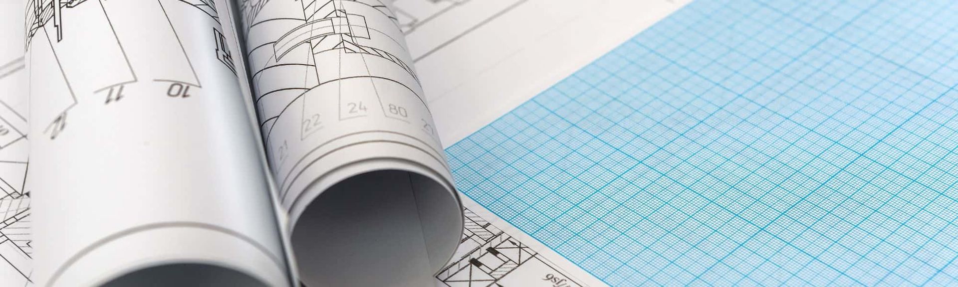 Two rolled-up architectural blueprints resting on a piece of light blue graph paper.
