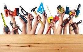 Several hands raised above a wooden plank, each holding a different construction tool like a drill, hammer, and level.
