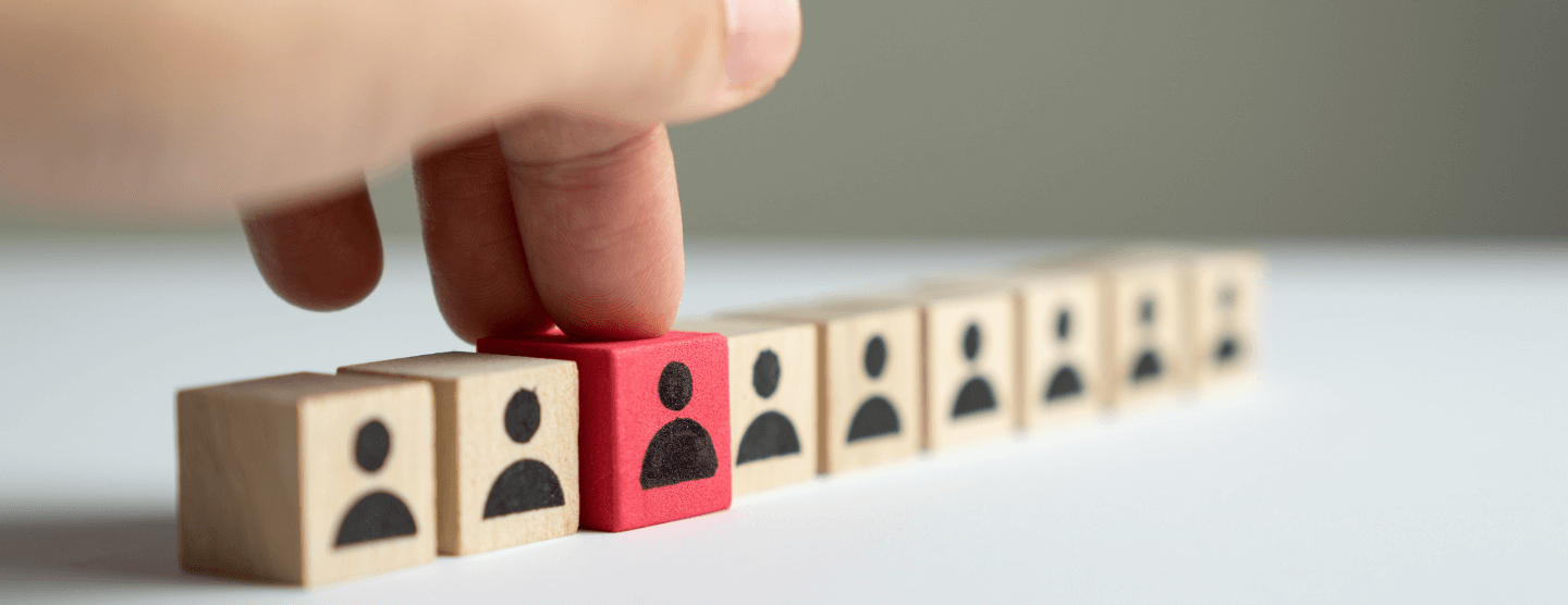 A hand places a red wooden block, marked with a person icon, into a line of identical, plain wooden blocks.