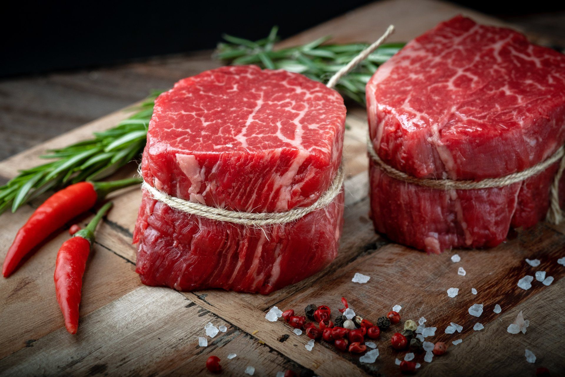 Two steaks are tied together with string on a wooden cutting board.