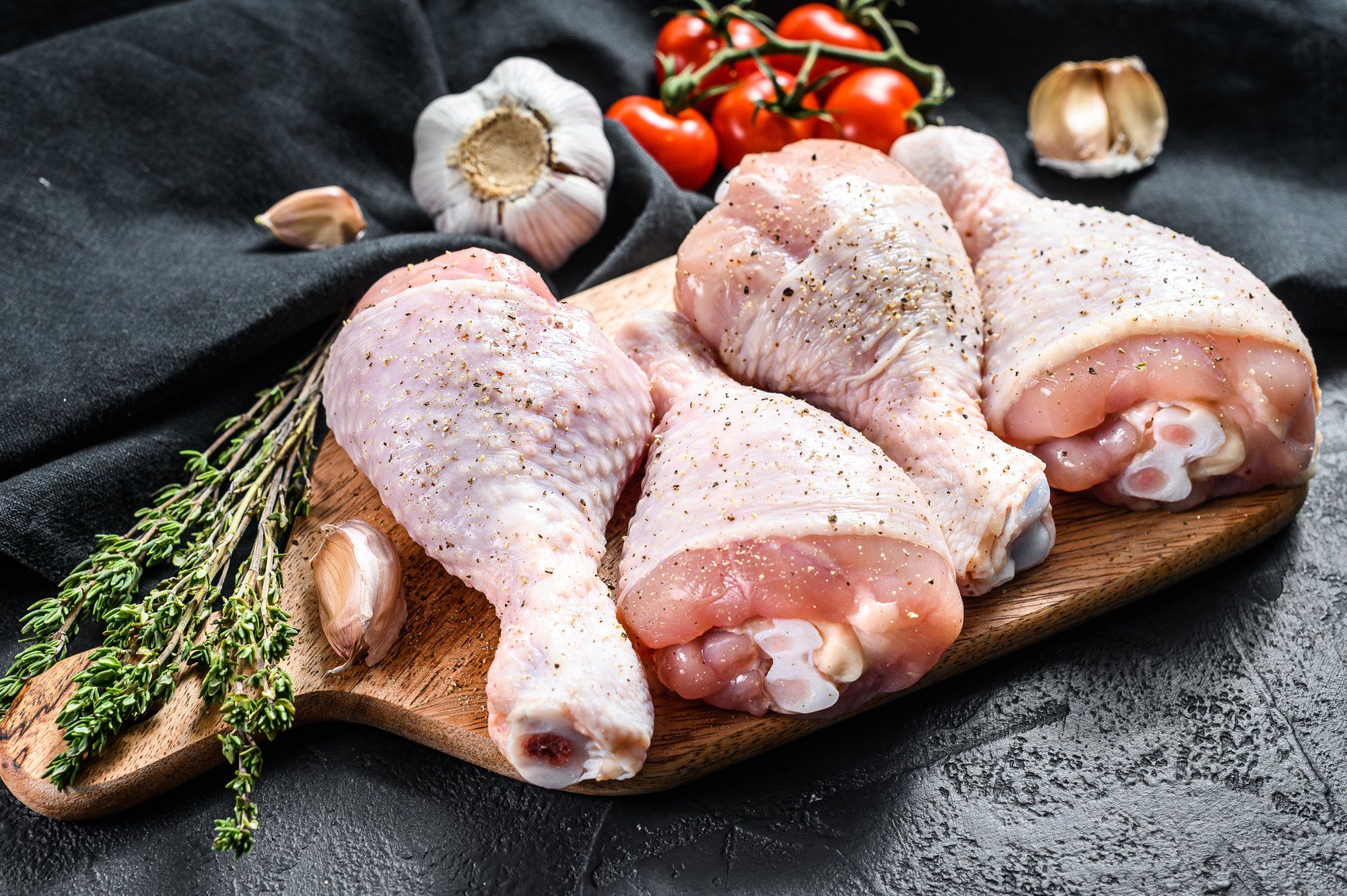 Raw chicken legs on a wooden cutting board with garlic and tomatoes.