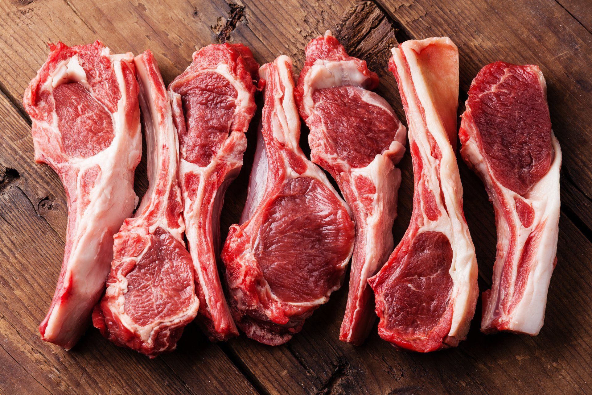 Raw lamb chops are arranged in a row on a wooden table.