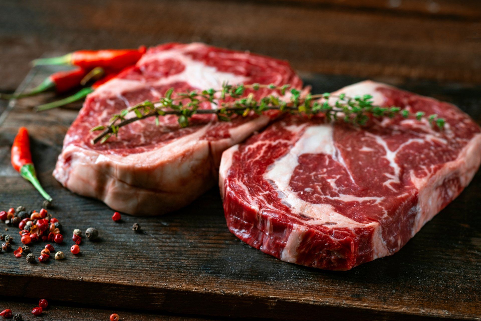 Two raw steaks are sitting on a wooden cutting board.