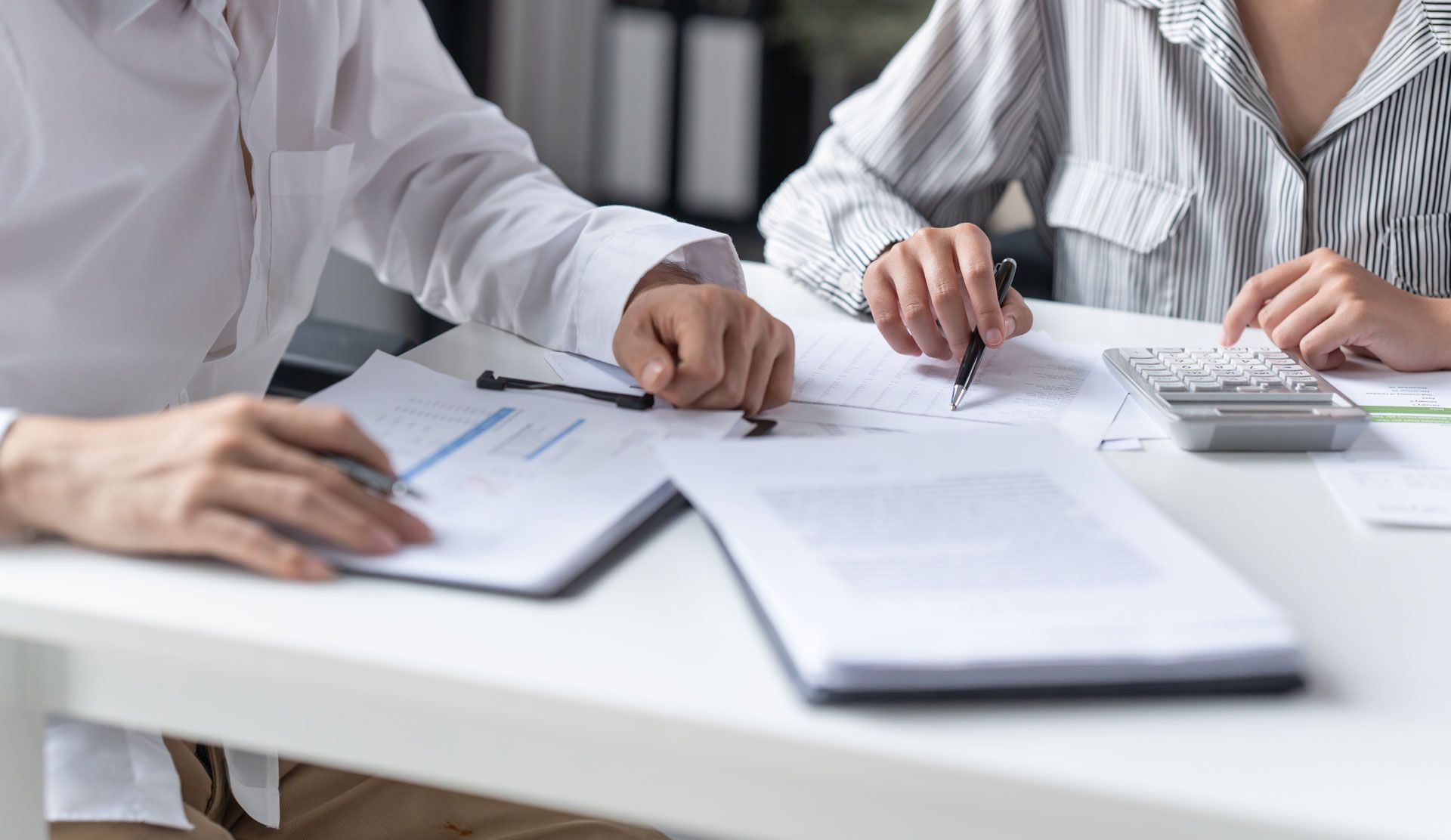 People reviewing documents at a bright office table with a calculator and notebooks
