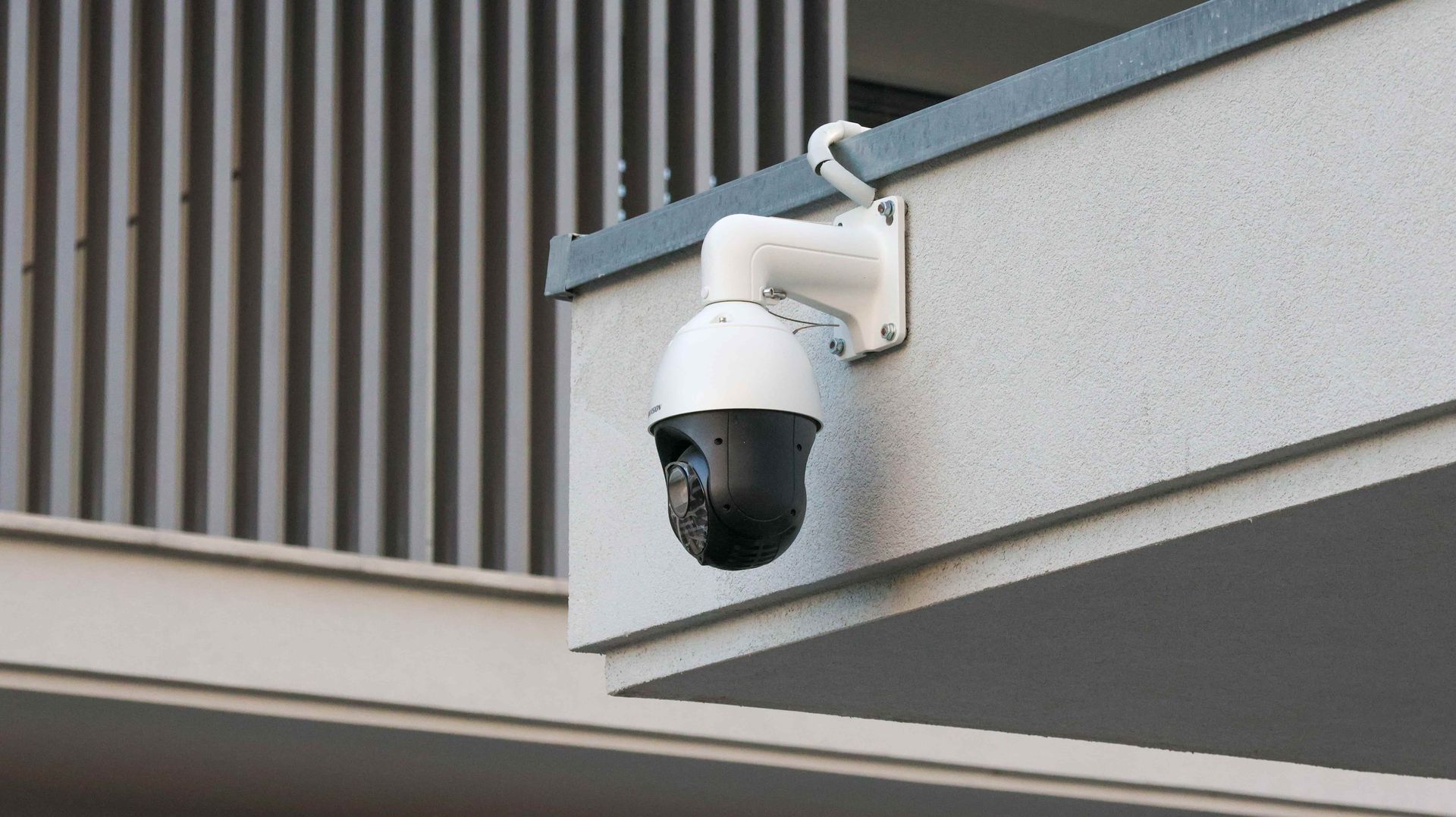 White security camera mounted on a building corner, aimed downward over the exterior wall