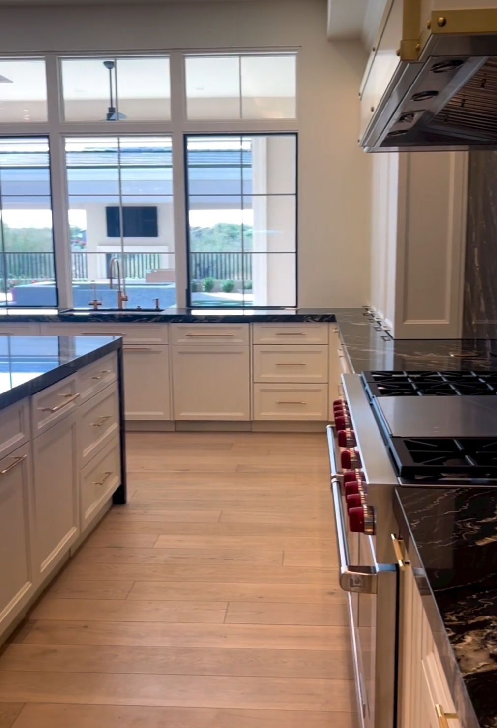 A kitchen with white cabinets , black counter tops , a stove , and a large window.