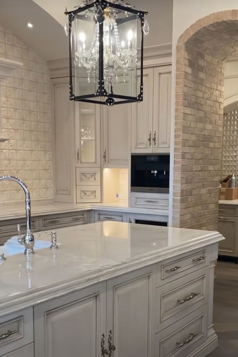 A kitchen with white cabinets and a large island with a chandelier hanging from the ceiling.