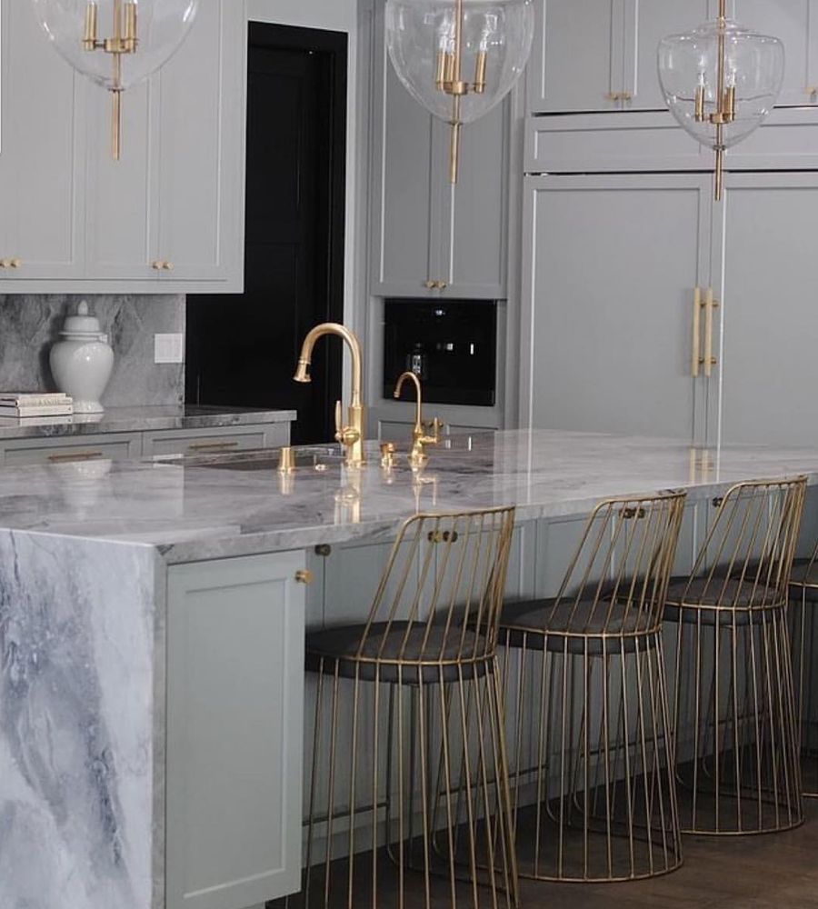 A kitchen with a marble counter top and gold chairs