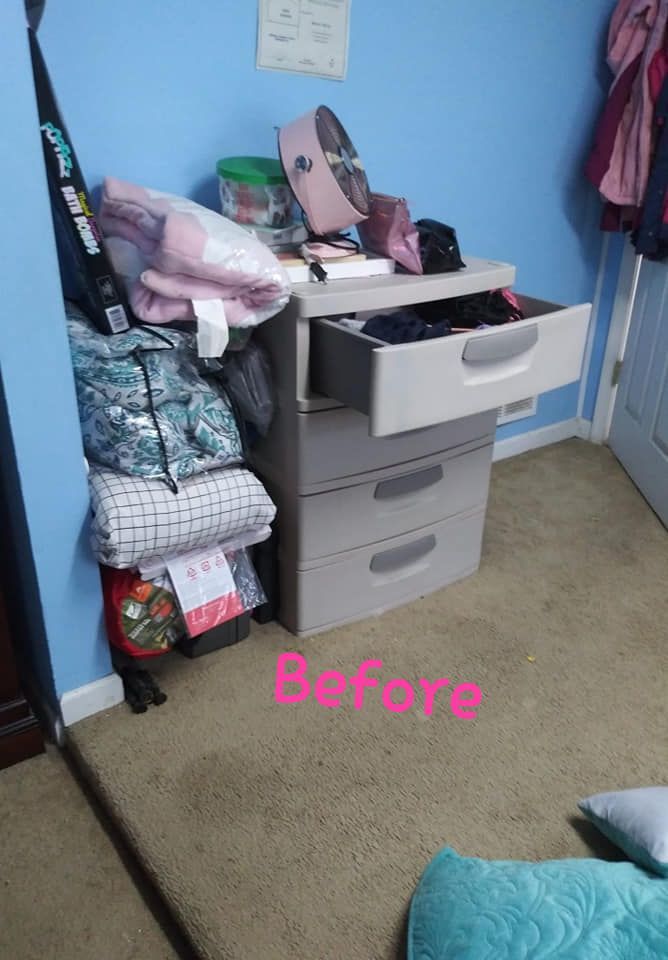 A cluttered dresser with an open drawer next to a pile of clothes and items in a blue-walled room.