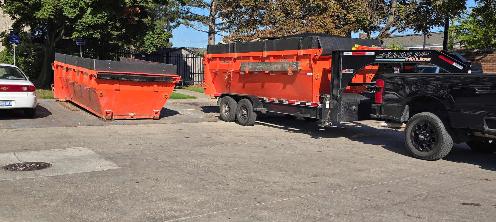 Orange dumpsters and a black truck on a paved surface.