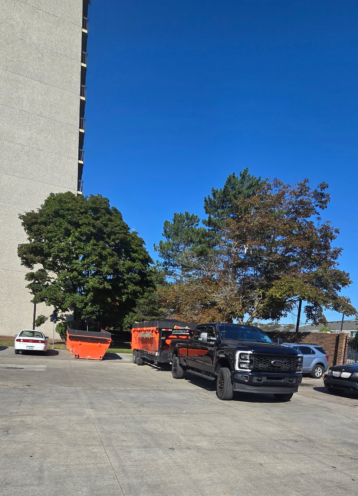 A black pickup truck towing equipment near a tall building, under a bright blue sky.