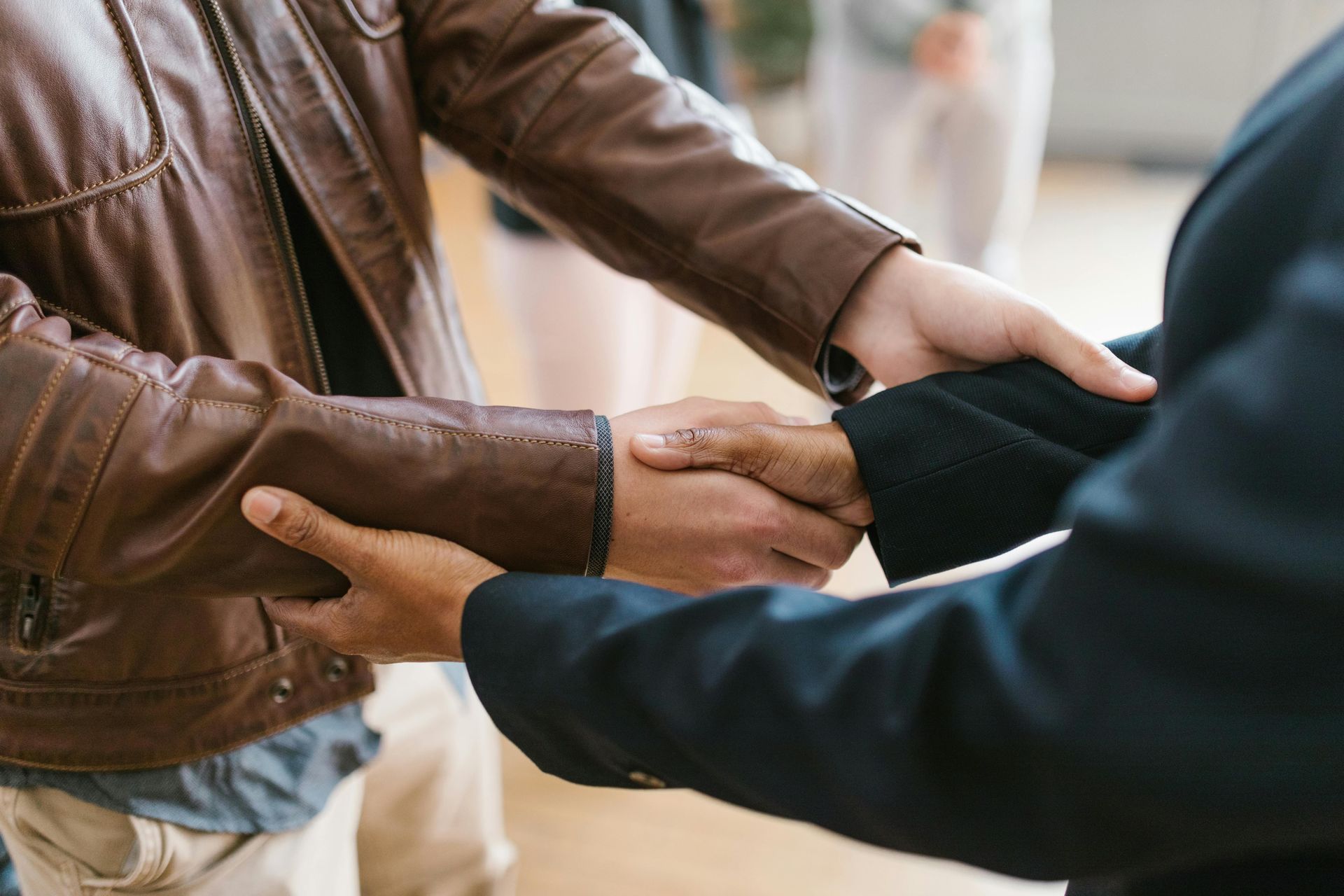 Two people shaking hands, one in a brown leather jacket, the other in a black blazer.