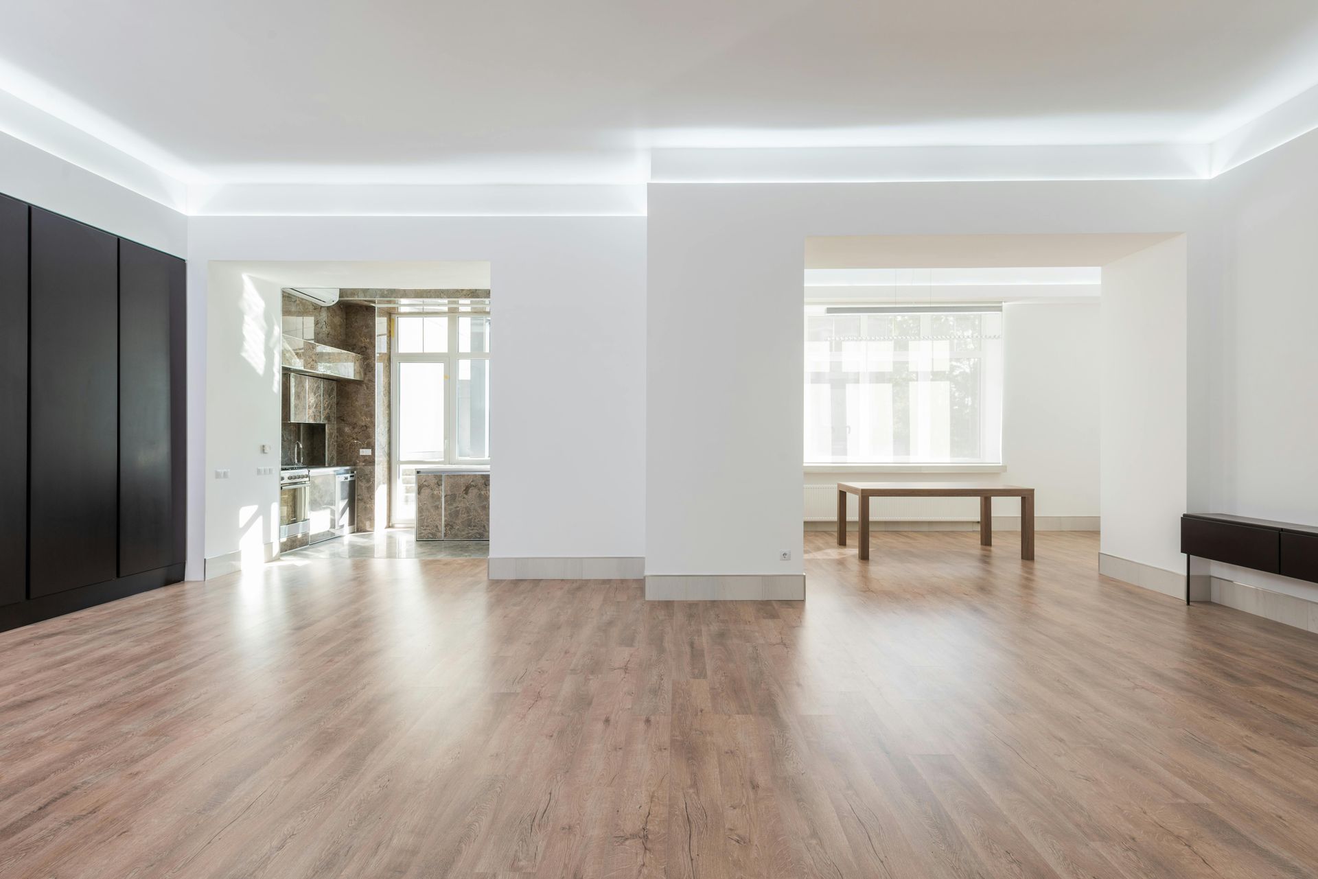 Modern, open-concept interior with wood floors, white walls, and dark cabinetry.  Kitchen and dining area visible.