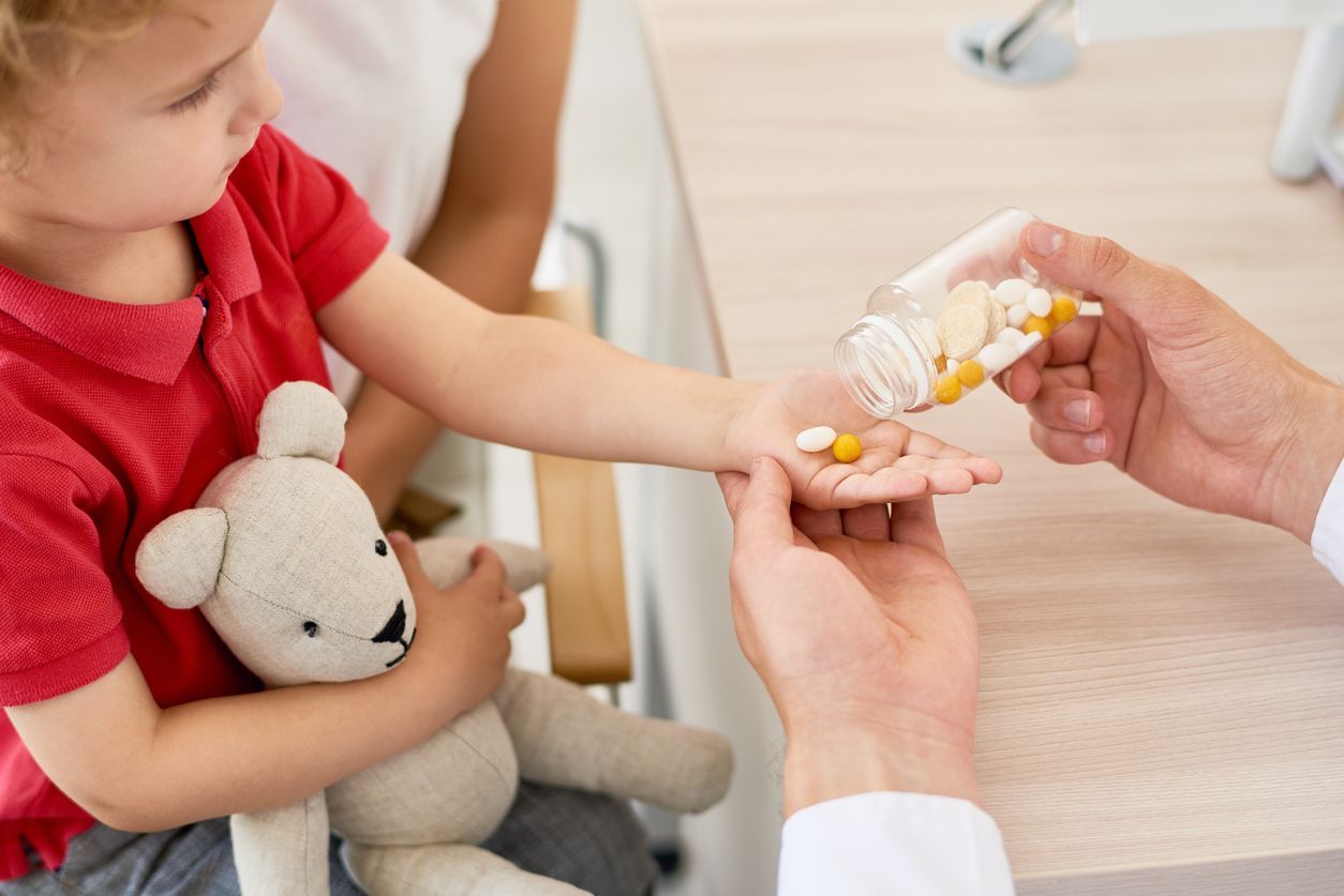 Una niña sostiene un osito de peluche y recibe pastillas de un médico.