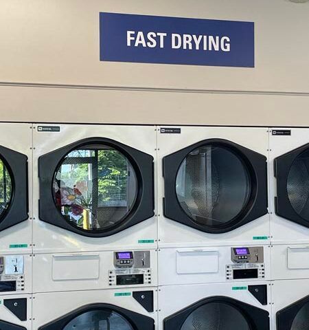 Row of white laundry dryers under a blue “FAST DRYING” sign in a laundromat