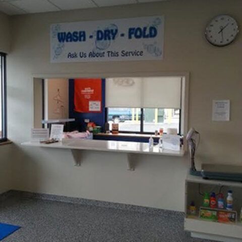 Wash-Dry-Fold service counter with a sign and pickup window in a laundromat