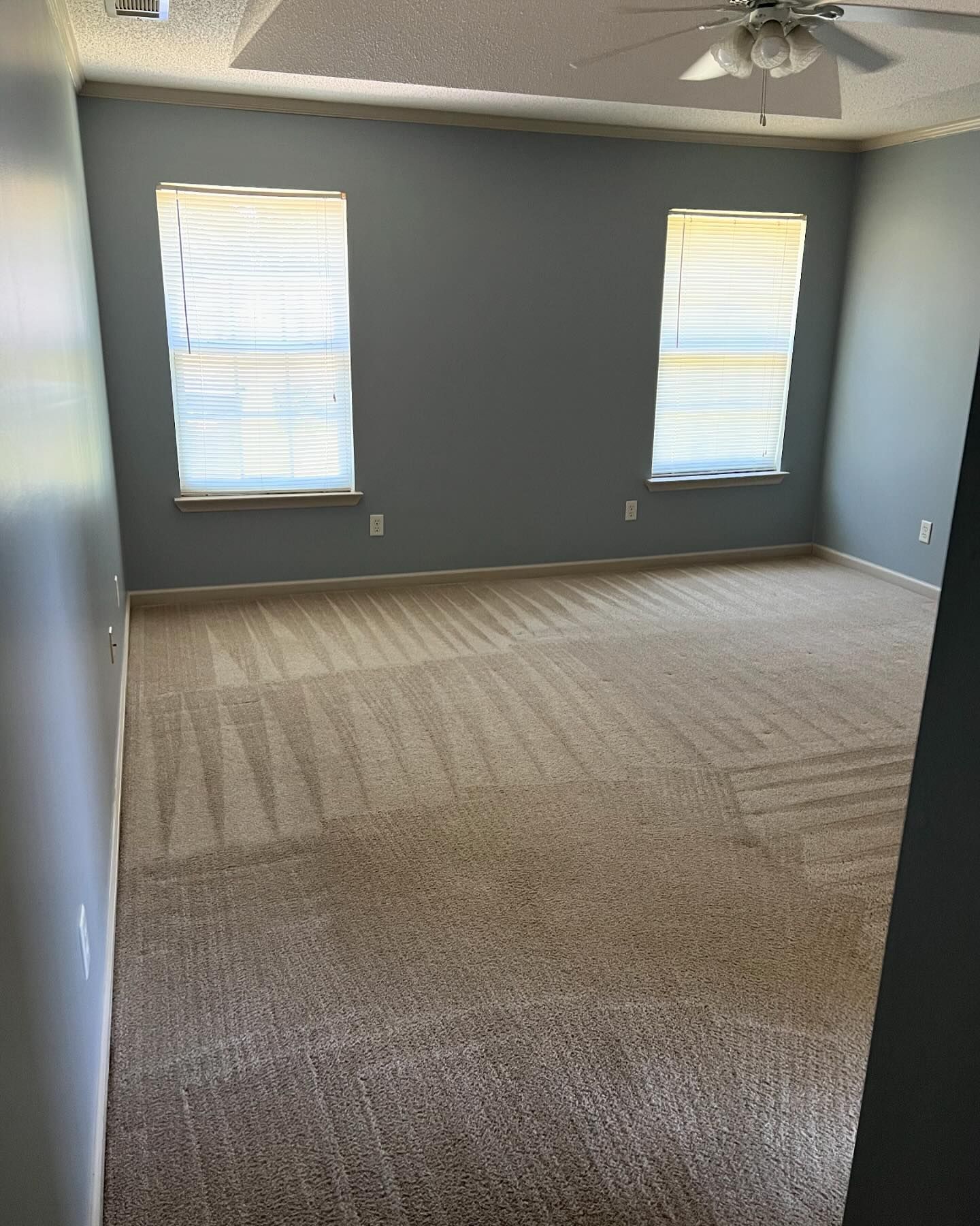 An empty bedroom with a ceiling fan and two windows.